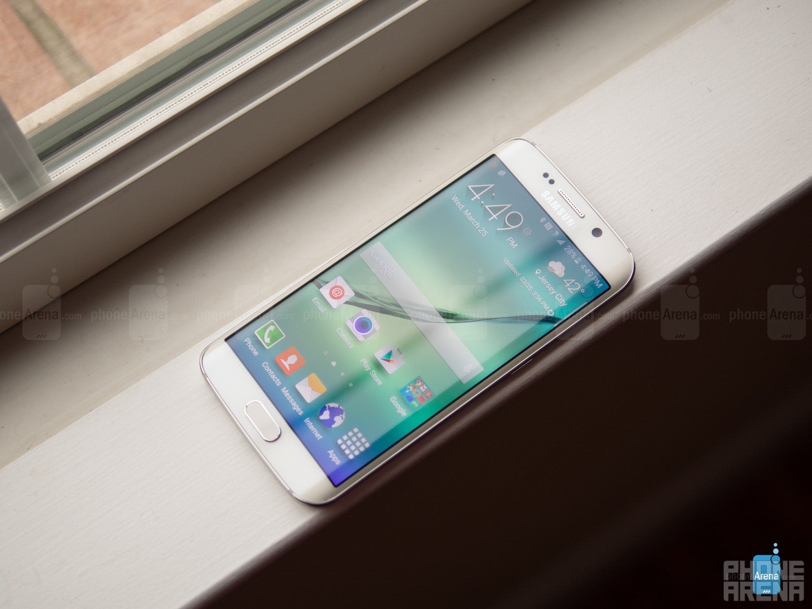 Samsung Galaxy S6 Edge که روی یک ویندوز قرار دارد ، که مستقیماً از بالا تصویر شده است. صفحه نمایش روشن است و صفحه اصلی را نشان می دهد